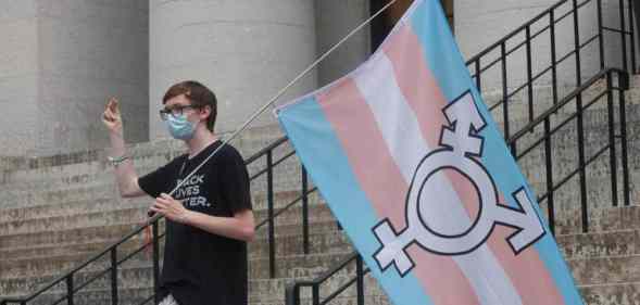 A protester holds the trans flag and snaps in solidarity with other speakers, during a trans rights demonstration
