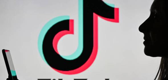 An image of a woman holding a cell phone in front of a TikTok logo displayed on a computer screen