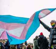 A person wearing a rainbow coloured face mask holds up a transgender Pride flag above their head
