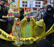 Joyce Chan (R) and Queenie Oyong (C) kneel down during the protest, holding circles with the rainbow flag