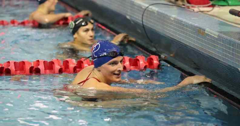 Lia Thomas clutches the side of a pool during a swimming meet and smiles at other competitors