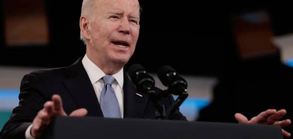 President Joe Biden, a white man, stands at a podium while wearing a dark suit jacket, white shirt and light blue tie