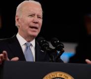 President Joe Biden, a white man, stands at a podium while wearing a dark suit jacket, white shirt and light blue tie