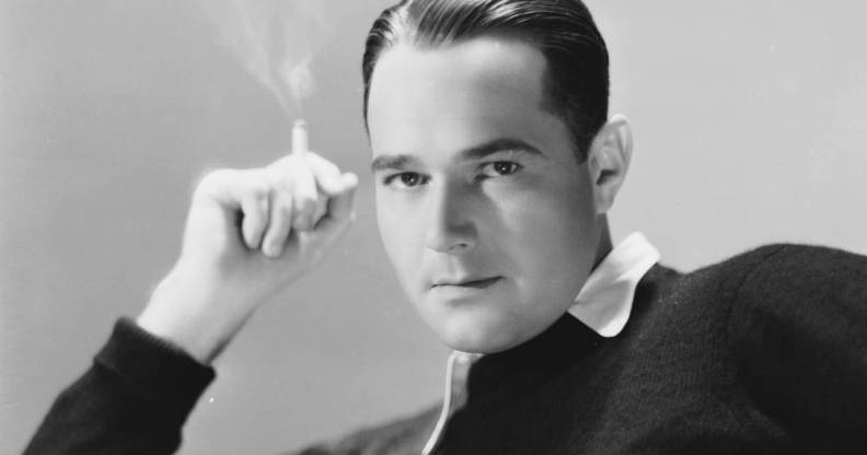 William Haines, an American actor, wears a white shirt and a dark sweater on top while holding a cigarette