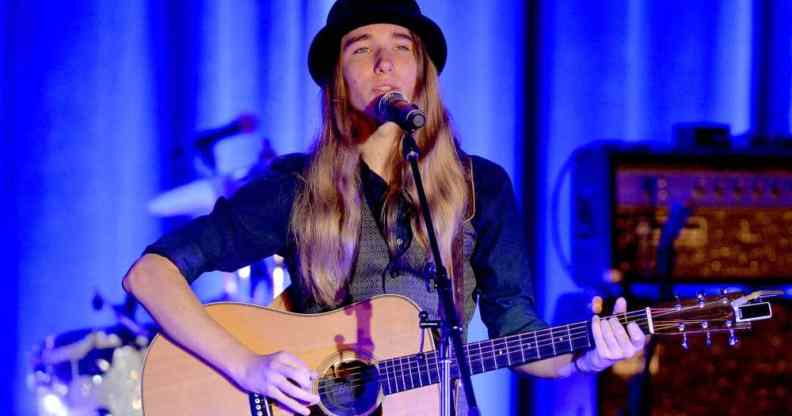 Sawyer Fredericks wears a bowler hat, grey vest and black long sleeved shirt as he sings and plays the guitar on stage