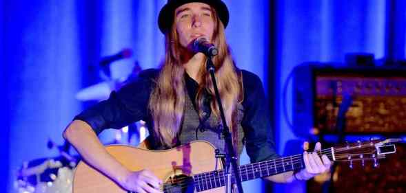Sawyer Fredericks wears a bowler hat, grey vest and black long sleeved shirt as he sings and plays the guitar on stage
