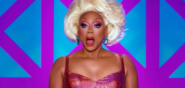 RuPaul in a pink dress and light blonde wig looking shocked