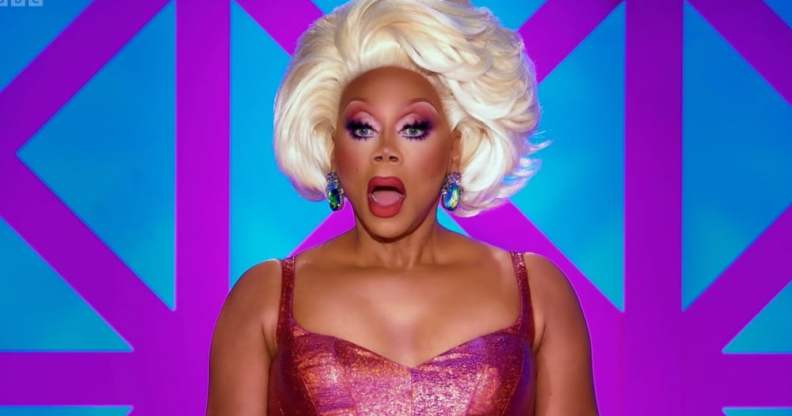 RuPaul in a pink dress and light blonde wig looking shocked