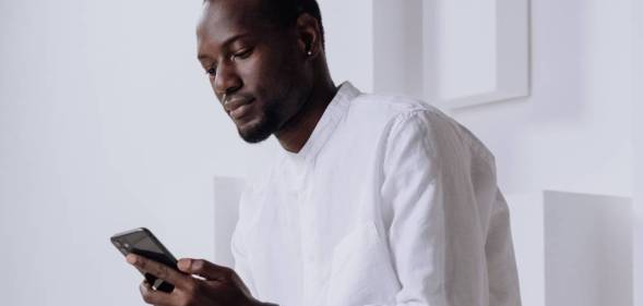 A Black person wears white as they use an Apple iPhone which has a digital assistant named siri