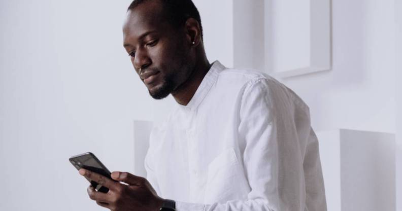 A Black person wears white as they use an Apple iPhone which has a digital assistant named siri