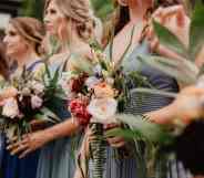 Several white women are standing next to each other while holding flowers as they act as bridesmaids in a wedding