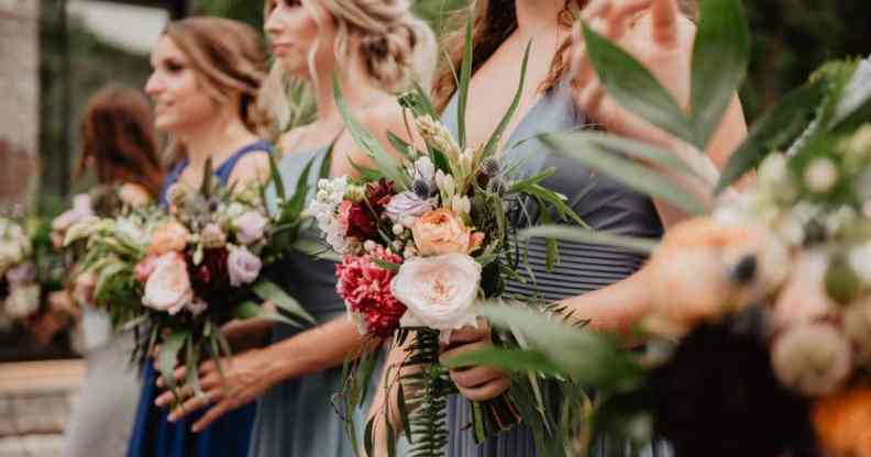 Several white women are standing next to each other while holding flowers as they act as bridesmaids in a wedding