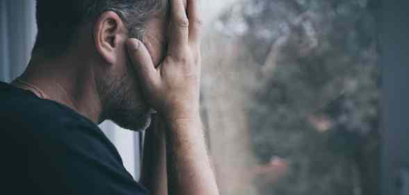 Man standing near a window and covers his face