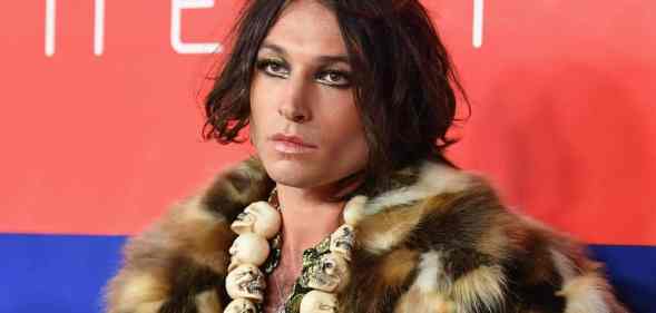 Actor Ezra Miller wears a fluffy brown fur-like jacket with a skull necklace and shiny makeup
