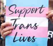 A placard that says 'support trans lives' printed against the transgender pride flag during a march