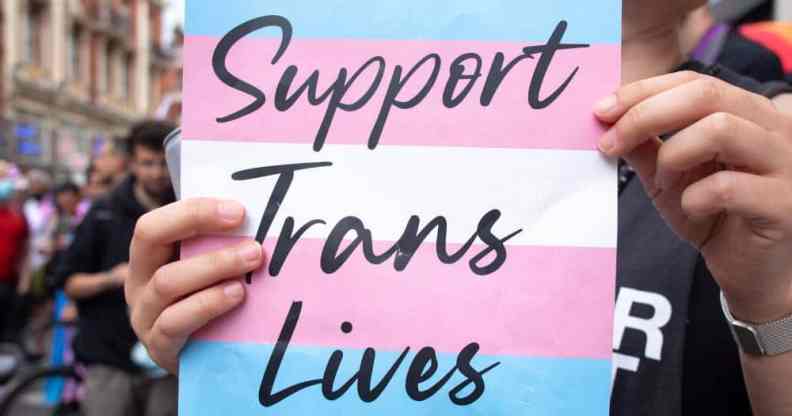 A placard that says 'support trans lives' printed against the transgender pride flag during a march