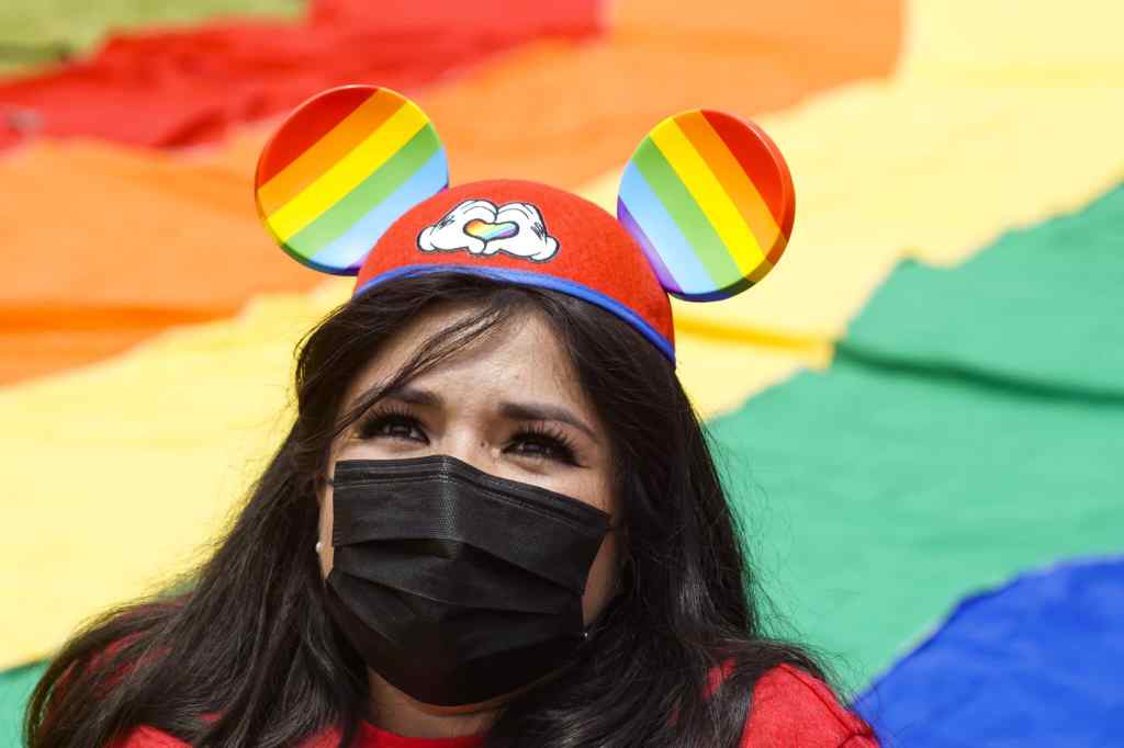 A woman wears Mickey Mouse ears with the Pride colours