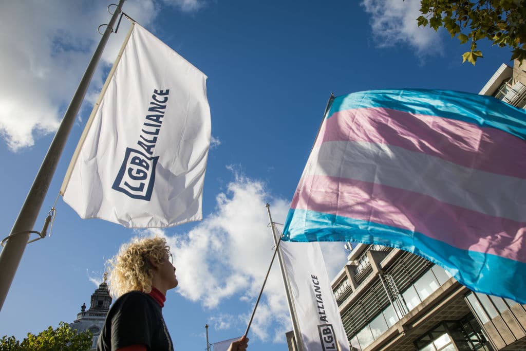 An activist holds a transgender pride flag at a protest by Transgender Action Block and supporters outside the first annual conference of the LGB Alliance at the Queen Elizabeth II Centre on 21st October 2021.