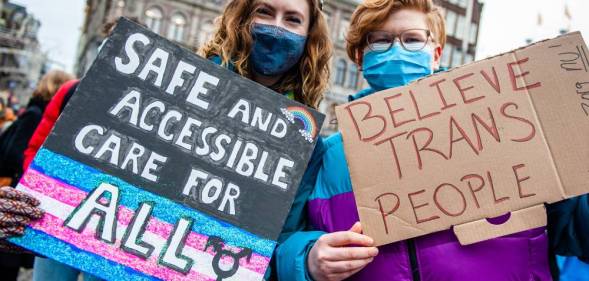 Two people hold placards in support of trans people