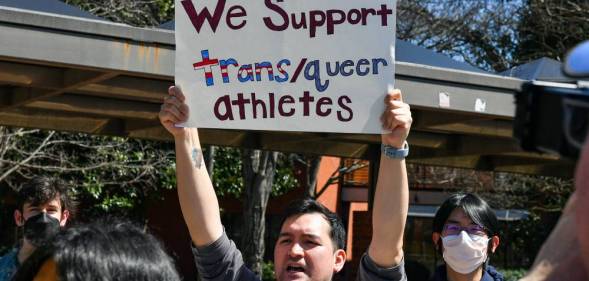 A person holds up a sign reading "We support trans/queer athletes" during a counter-protest