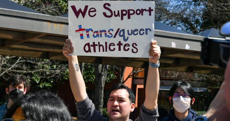 A person holds up a sign reading "We support trans/queer athletes" during a counter-protest