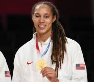 Brittney Griner, a basketball player, holds up her Olympic gold medal while wearing a white Team USA jacket