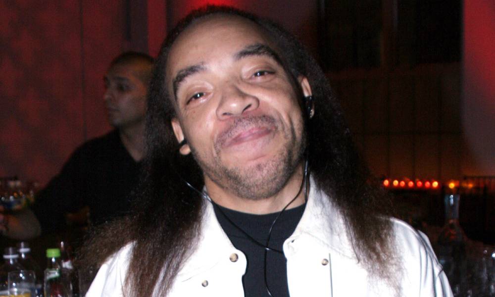 Kidd Creole, a rapper, smiles at the camera while wearing a black top and white jacket