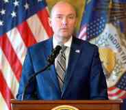 Utah governor Spencer Cox wears a blue suit, white shirt and grey striped tie while speaking at a press conference