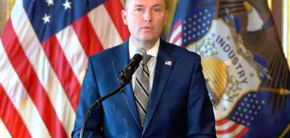 Utah governor Spencer Cox wears a blue suit, white shirt and grey striped tie while speaking at a press conference