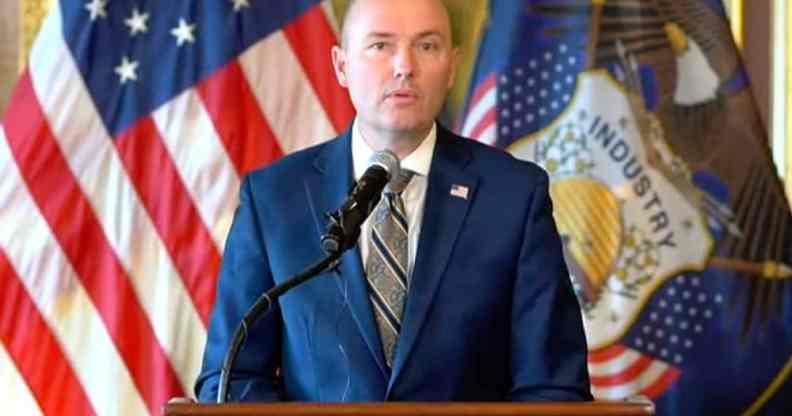 Utah governor Spencer Cox wears a blue suit, white shirt and grey striped tie while speaking at a press conference