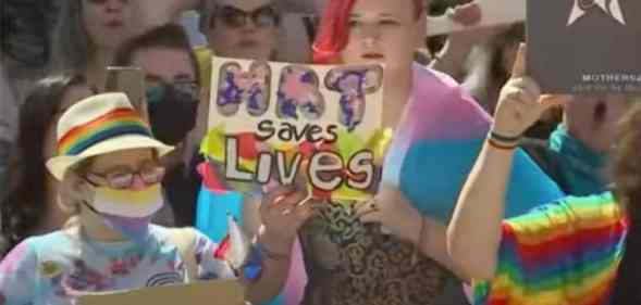 A person holds a sign up in support of the trans community that reads "HRT saves lives" amid protests in Texas