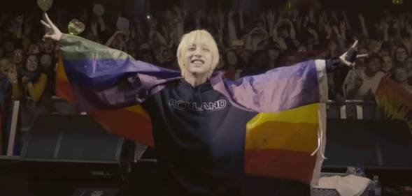 Korean singer Holland wears an LGBT+ flag as he performs on stage with a crowd of fans behind him