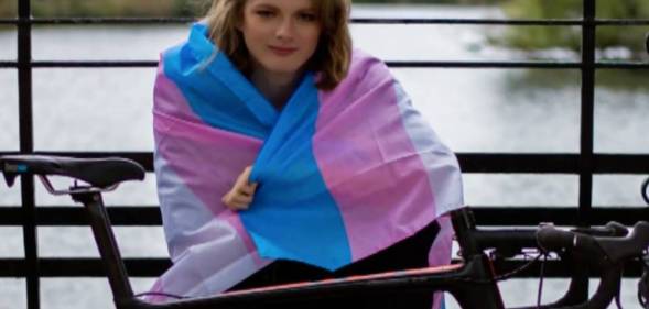 Cyclist Emily Bridges wears a trans flag around her shoulders as she sits behind a bicycle