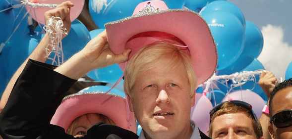 Boris Johnson wearing a pink stetson in front of blue, pink and white balloons
