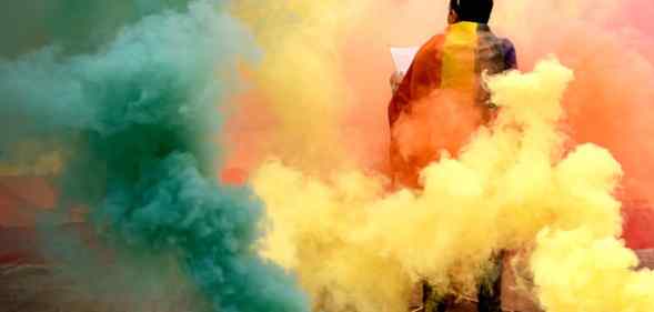 A person stands among multicoloured smoke