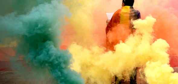 A person stands among multicoloured smoke