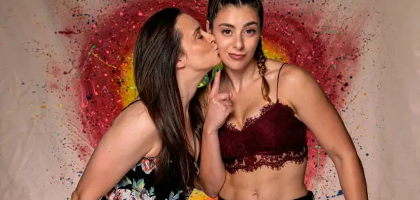 PROGRESS Wrestling stars Jetta and Charlie Morgan, a British LGBT+ couple and wrestlers, hold each other close with a rainbow heart in the background