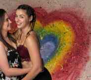 Jetta and Charlie Morgan, a British LGBT+ couple and wrestlers, hold each other close with a rainbow heart in the background