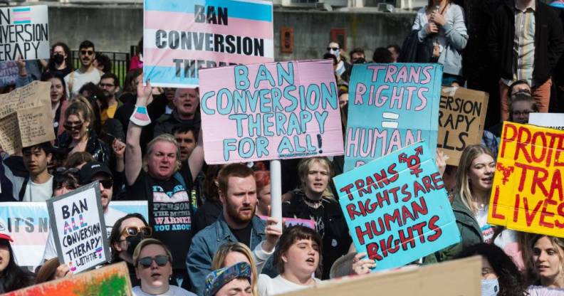 Crowd of people gather in protest of the UK government's U-turn on conversion therapy ban and hold up signs in support of protections for the trans community