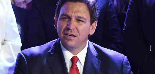 Ron DeSantis is seen wearing a suit and tie while surrounded by others