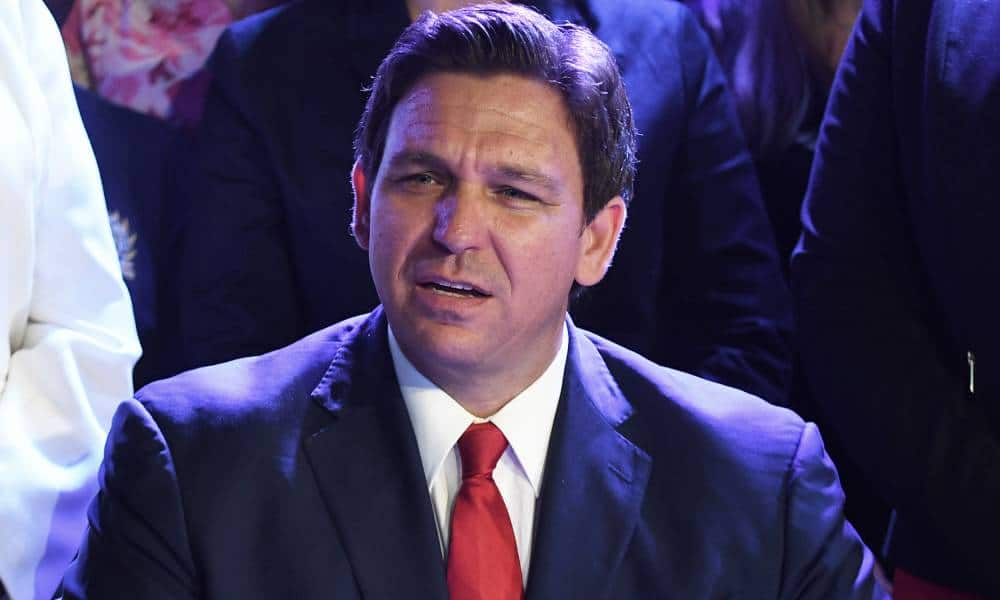 Ron DeSantis is seen wearing a suit and tie while surrounded by others