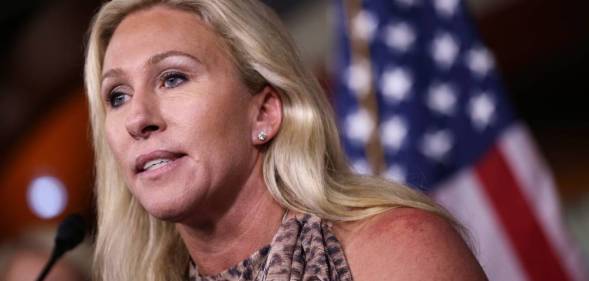 Marjorie Taylor Greene speaks into a microphone while an American flag can be seen in the background