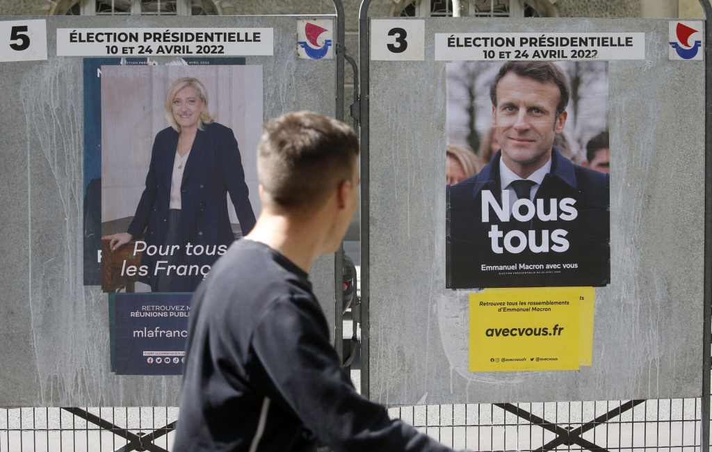 A man walks past official campaign posters of Marine Le Pen Emmanuel Macron