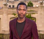 Jerrod Carmichael stares at the camera while wearing a black shirt and a dark red jacket