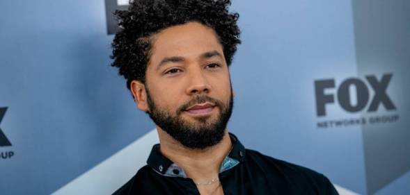 Jussie Smollett stares off camera while wearing a dark shirt with blue elements on the collar