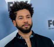 Jussie Smollett stares off camera while wearing a dark shirt with blue elements on the collar