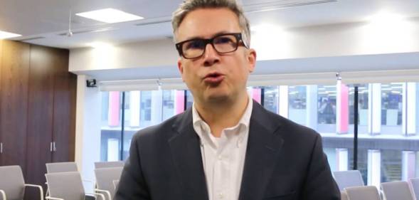 Iain Anderson wears a white shirt and black suit jacket as he looks at the camera