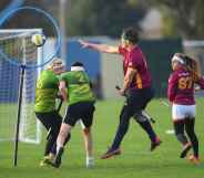 A real game of quidditch - here are four players with sticks between their legs (like broomsticks), one is jumping while throwing a ball into a hoop