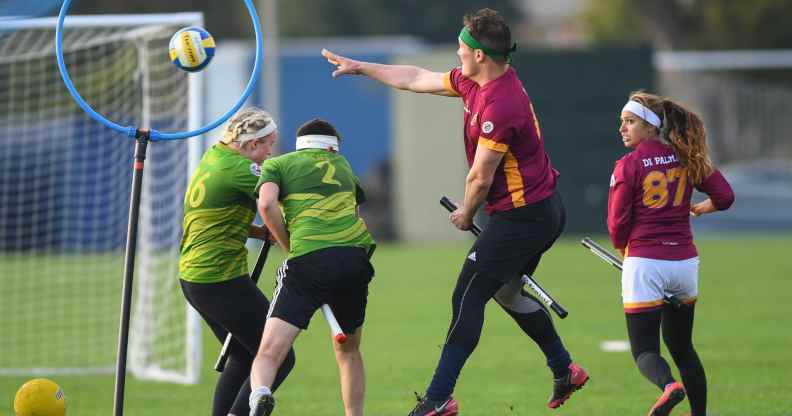 A real game of quidditch - here are four players with sticks between their legs (like broomsticks), one is jumping while throwing a ball into a hoop