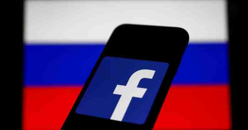 Facebook logo displayed on a phone screen and Russian flag displayed on a screen in the background